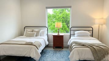 Une chambre avec deux lits, une fenêtre donnant sur la forêt, une table de chevet avec une lampe et un tapis bleu à motifs.
