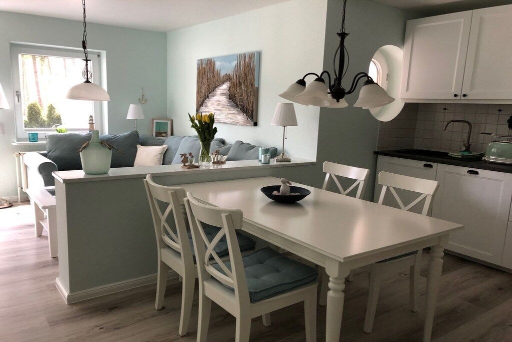 A dining area with a white table and chairs, a kitchen with white cabinets, and a painting on the wall.