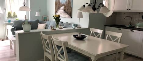 A dining area with a white table and chairs, a kitchen with white cabinets, and a painting on the wall.