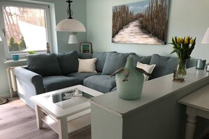 A living room with a grey sofa, a white coffee table, and a painting of a beach path. - Holiday apartment with 2 bedrooms (Hohwacht)