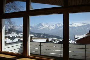 A view through a window with a mountain landscape, including snow-covered peaks and a village below. - Holiday apartment with 2 bedrooms (Beatenberg)