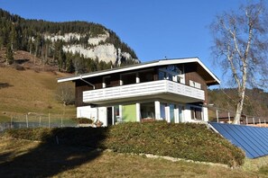 A modern two-story house with a balcony, surrounded by a fenced yard, set against a mountainous backdrop. - Holiday apartment with 2 bedrooms (Beatenberg)