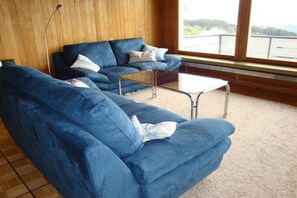 A room with two blue sofas, a small table, and a view through a window. - Holiday apartment with 2 bedrooms (Beatenberg)