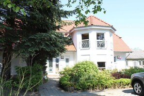 A two-story building with a red-tiled roof, a balcony with a metal railing, and a paved driveway leading to the entrance. - with bay window - close to the Zingst harbor (Zingst)