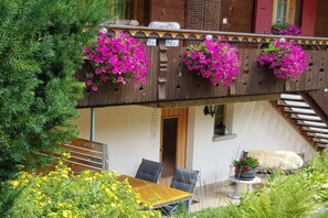 A balcony with hanging flower baskets, a wooden table with chairs, and a staircase leading to an upper level. - Holiday apartment with 2 bedrooms (Grindelwald)