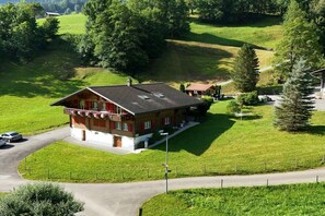 A two-story building with a sloped roof, surrounded by green fields and trees. - Holiday apartment with 2 bedrooms (Grindelwald)