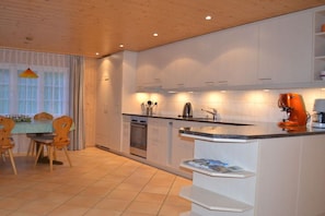 A modern kitchen with white cabinetry, a built-in oven, and a dining area with wooden chairs and a table. - Holiday apartment with 2 bedrooms (Grindelwald)