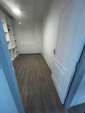 Ein schmaler Flur mit Holzboden, einer weißen Tür und einer weißen Wand mit einer eingelassenen Deckenleuchte.
