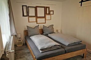 Uma cama de casal com roupa de cama cinza, cabeceira de madeira e luminária fixada na parede.