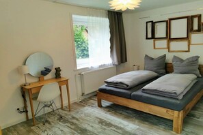 A bedroom with a wooden bed, a desk with a chair, a round mirror, and a window with curtains. - Pastorate Garden Schlei (Norderbrarup)