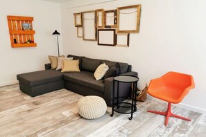 Ein modernes Wohnzimmer mit einer Eckcouch, einem runden Couchtisch und einem leuchtend orangefarbenen Sessel.
