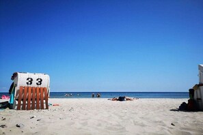 A beach with a row of beach chairs and a beach umbrella, a clear blue sky, and the ocean in the background. - Pastorate Garden Schlei (Norderbrarup)