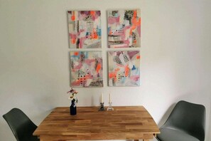 A dining area with a wooden table, four abstract paintings on the wall, and two chairs. - Pastorate Garden Schlei (Norderbrarup)