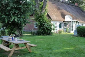 A rustic thatched-roof house with a picnic table set up in the yard. - Pastorate Garden Schlei (Norderbrarup)