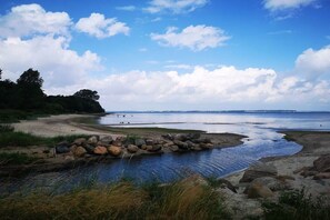 Eine Küstenlandschaft mit ruhigem Gewässer, Sandstrand und felsiger Küste.
