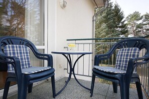 Zwei Stühle mit Karokissen, ein kleiner runder Tisch und ein Metallgeländer auf einem Balkon mit einem Gebäude im Hintergrund.