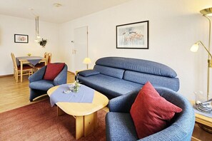 Ein modernes Wohnzimmer mit einem blauen Sofa, einem Holztisch und einem Essbereich mit Tisch und Stühlen.