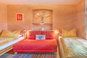 A room with two beds, a central sofa, a small table with a vase, and a framed picture on the wall. - Holiday apartment with 2 bedrooms (Angath)
