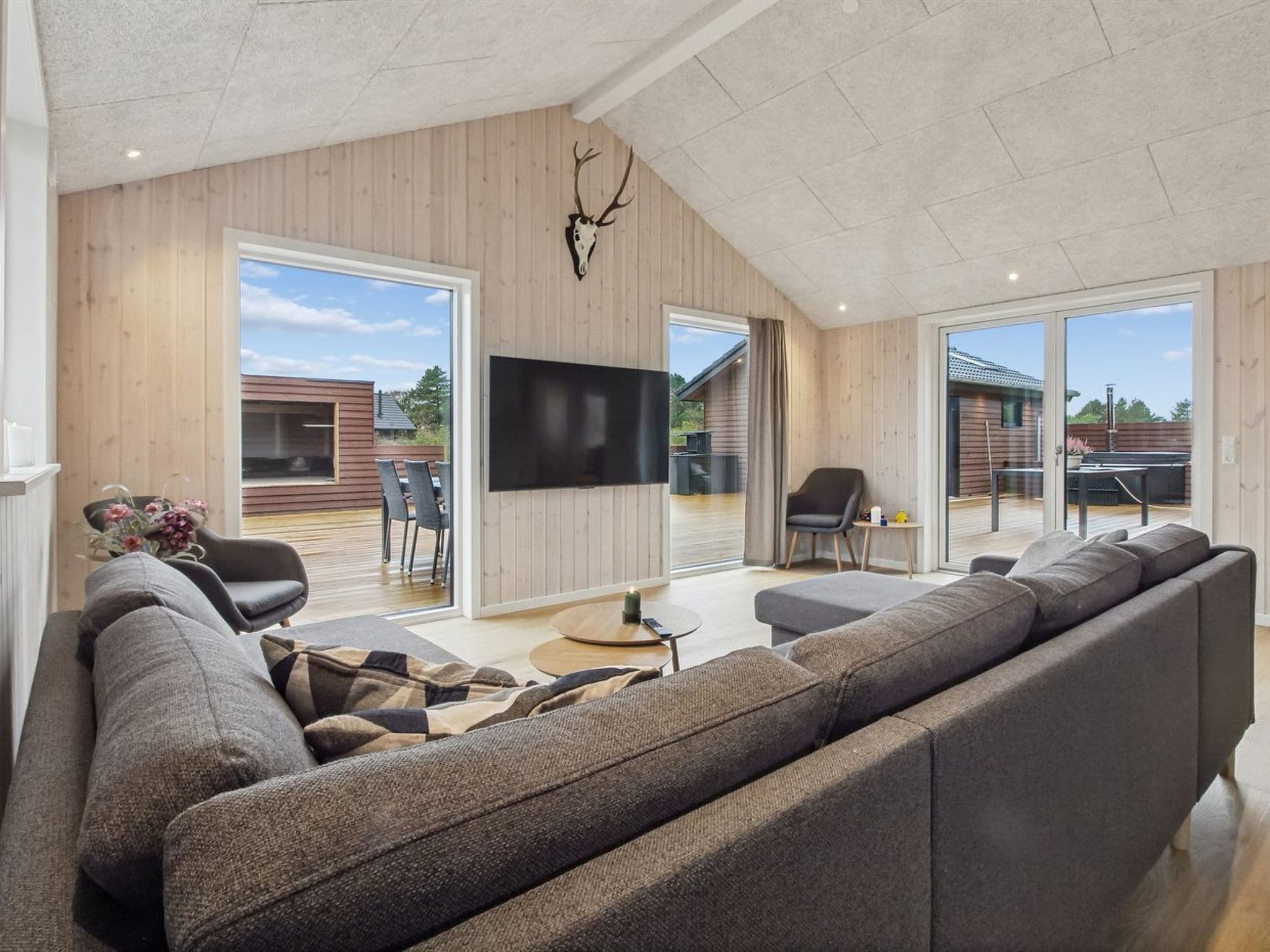 A modern living room with a large sofa, a flat-screen TV, and a wooden ceiling.