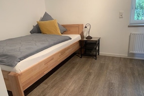 Ein Einzelbett mit Holz-Kopfteil und einem Nachttisch mit Lampe.