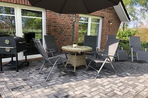 Eine Außenpatio mit einer Ziegelwand, einem runden Tisch, vier Stühlen, einem Grill und einem Sonnenschirm.
