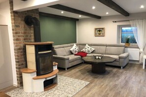 Ein Wohnzimmer mit Kamin, einer Couch, einem Couchtisch und Blick ins Freie.