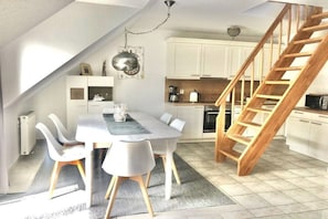 Una cucina moderna con mobili bianchi, una scala in legno e un'area pranzo con tavolo e sedie.