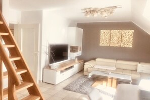 Ein modernes Wohnzimmer mit Flachbildfernseher, einer Couch, einem Couchtisch und einer Treppe.