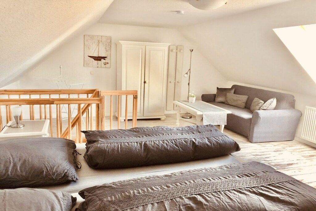 A cozy loft bedroom with a sloped ceiling, a wooden crib, a grey sofa, and a white wardrobe.