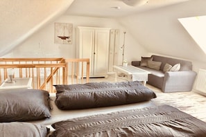 Ein gemütliches Schlafzimmer im Loft-Stil mit schrägem Dach, einem Holckbett, einem grauen Sofa und einem weißen Kleiderschrank.