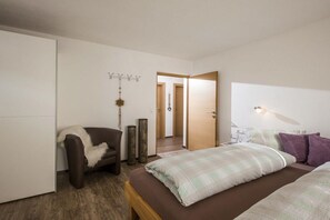 Ein Schlafzimmer mit Bett, Stuhl, Kleiderständer und einer Tür zu einem anderen Raum.