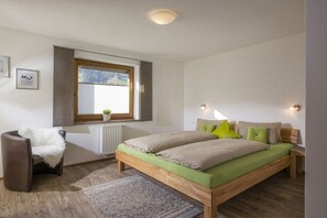 A bedroom with a wooden bed, a window with blinds, a radiator, a chair with a blanket, and a small plant. - Holiday apartment with 2 bedrooms (Ramsau im Zillertal)