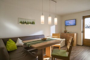 A modern living room with a wooden dining table, a sofa, and a TV mounted on the wall. - Holiday apartment with 2 bedrooms (Ramsau im Zillertal)
