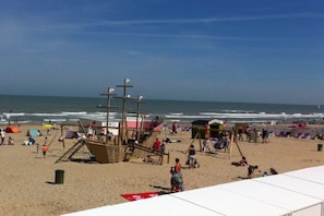 Een strand met een reddingstoren, strandparasols en een zandgebied met mensen.