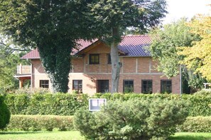 A two-story brick building with a red-tiled roof, a balcony on the second floor, and a well-maintained hedge in the foreground. - Holiday apartment in Saal with swimming pool (Saal)