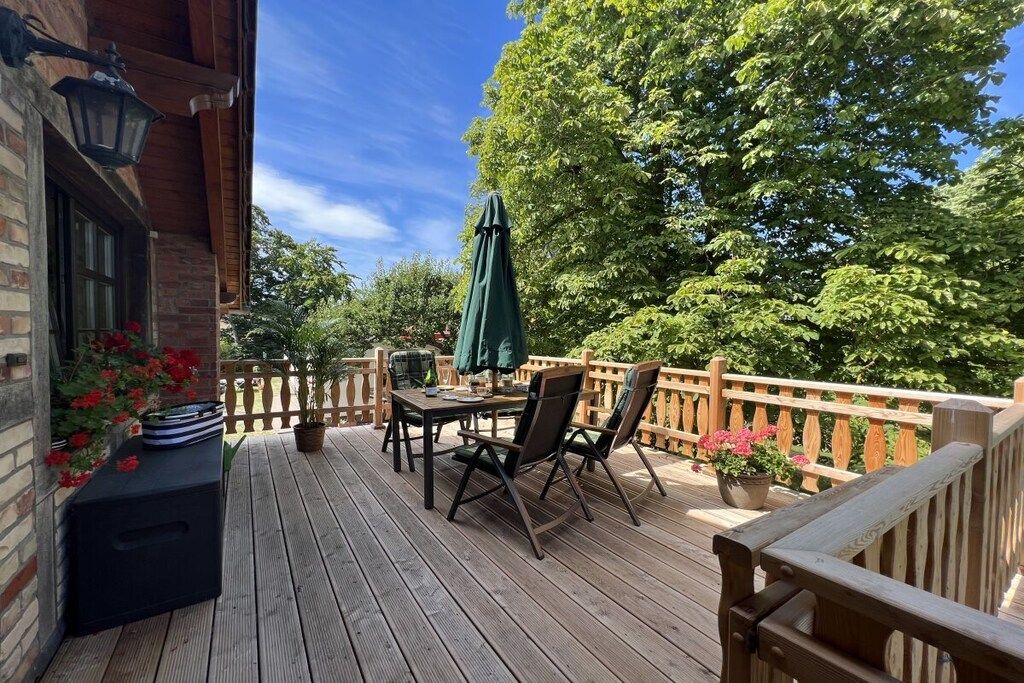 A wooden deck with a table and chairs, surrounded by a wooden railing and potted plants.