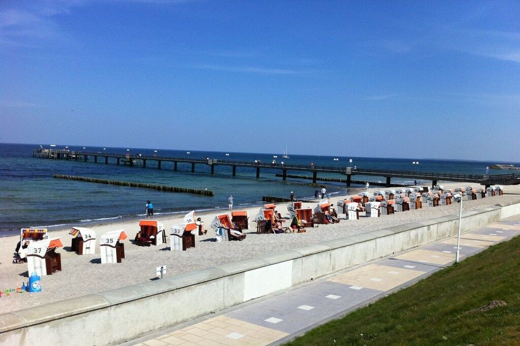 En strand med numrerade strandhytter och en pir i bakgrunden.