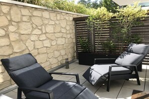 A patio area with two black lounge chairs and a stone wall. - Holiday apartment with 1 bedroom (Kühlungsborn)