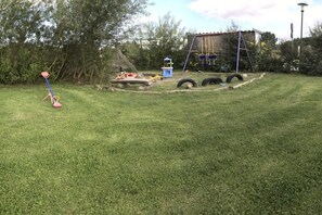 A grassy outdoor area with a swing set, a play structure, and a tire obstacle course. - Holiday home with 2 bedrooms (Neuendorf)