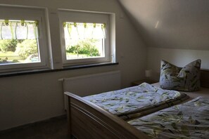 A bedroom with a bed, a window with curtains, a radiator, and a pillow with a leaf pattern. - Holiday apartment with 1 bedroom (Struppen)
