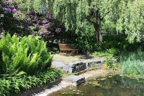 A garden with a wooden bench, a stone bridge, and lush greenery. - Holiday apartment with 1 bedroom (Struppen)