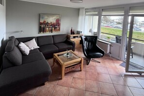 A living room with a sofa, a coffee table, a chair, and a painting on the wall. - Villa by the sea Apt. 39 (Grömitz)