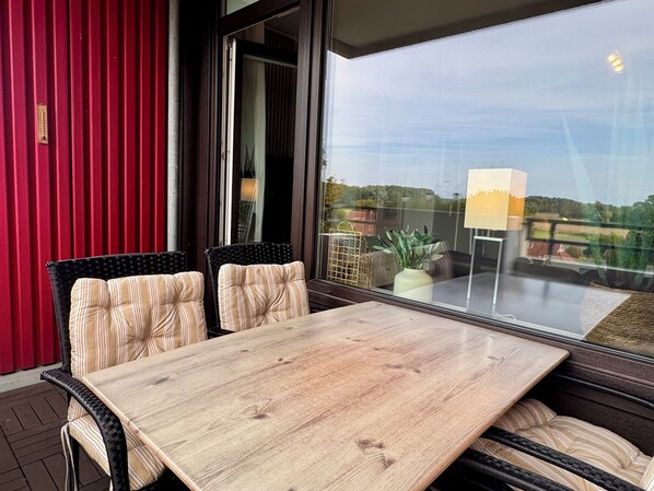 Un balcón con mesa y sillas de madera, una pared roja y vistas al campo.
