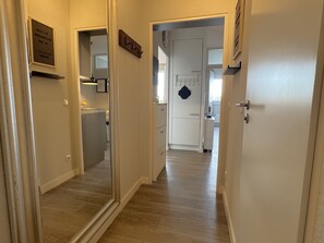 Un pasillo con piso de madera, una puerta con placa y una zona de cocina al fondo.