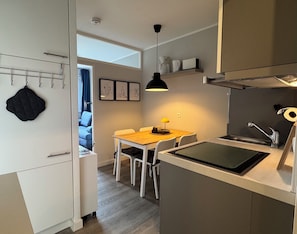 Cocina compacta con comedor, una lámpara colgante negra y vistas hacia la sala.