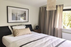 A neatly made bed with a white and gray striped bedspread, a black headboard, and a framed picture on the wall. - Holiday home in Ballum with swimming pool (Ballum)