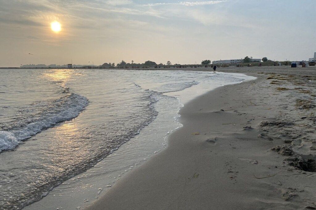 A beach with gentle waves, a clear sky, and a distant shoreline with buildings.