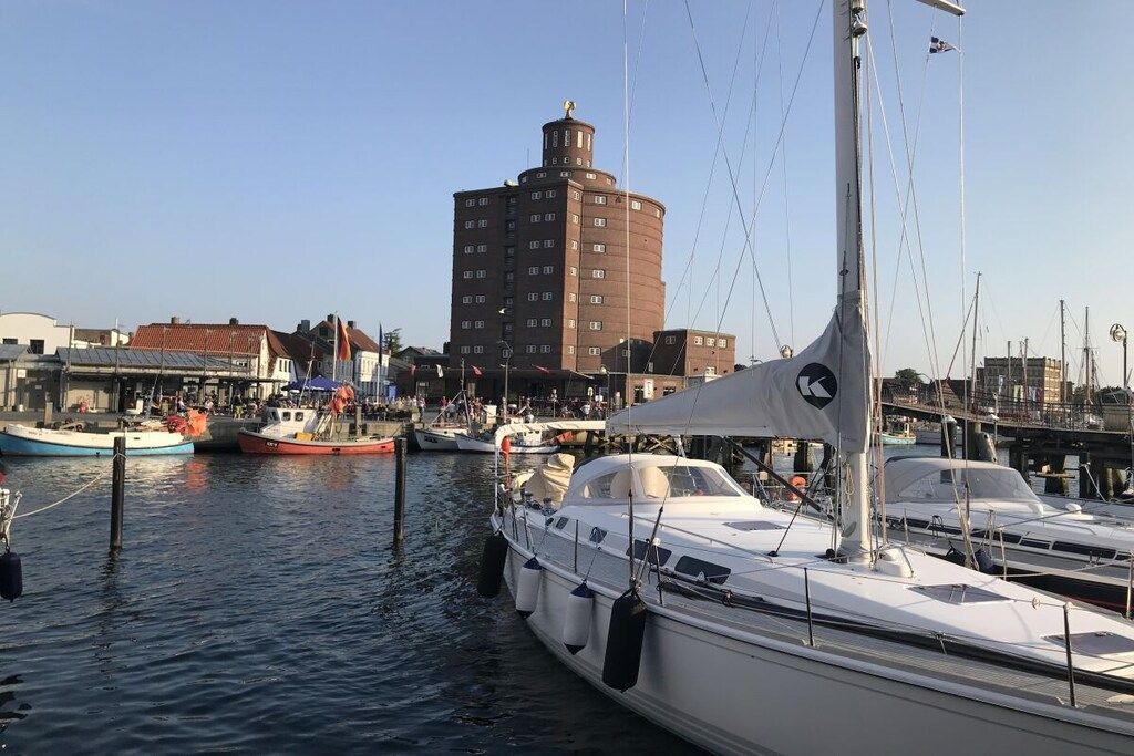 Uma marina com barcos atracados, um edifício imponente com topo arredondado e céu claro.