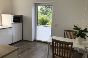 Eine kleine Küche mit einer Mikrowelle, ein Essbereich mit Tisch und Stühlen sowie ein Blick ins Freie durch eine Tür.