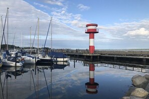 Ein Hafen mit vertäuten Booten, einem Leuchtturm und ruhigem Wasser, das den Himmel spiegelt.
